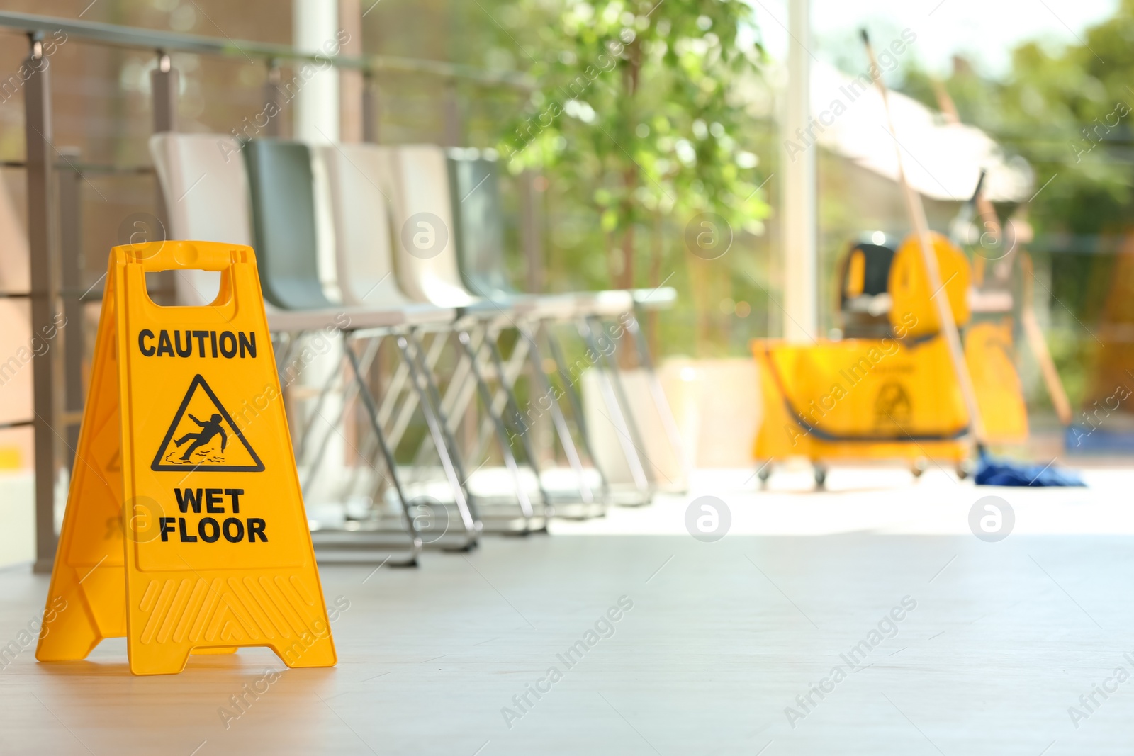 Photo of Safety sign with phrase Caution wet floor and blurred mop bucket on background. Cleaning service