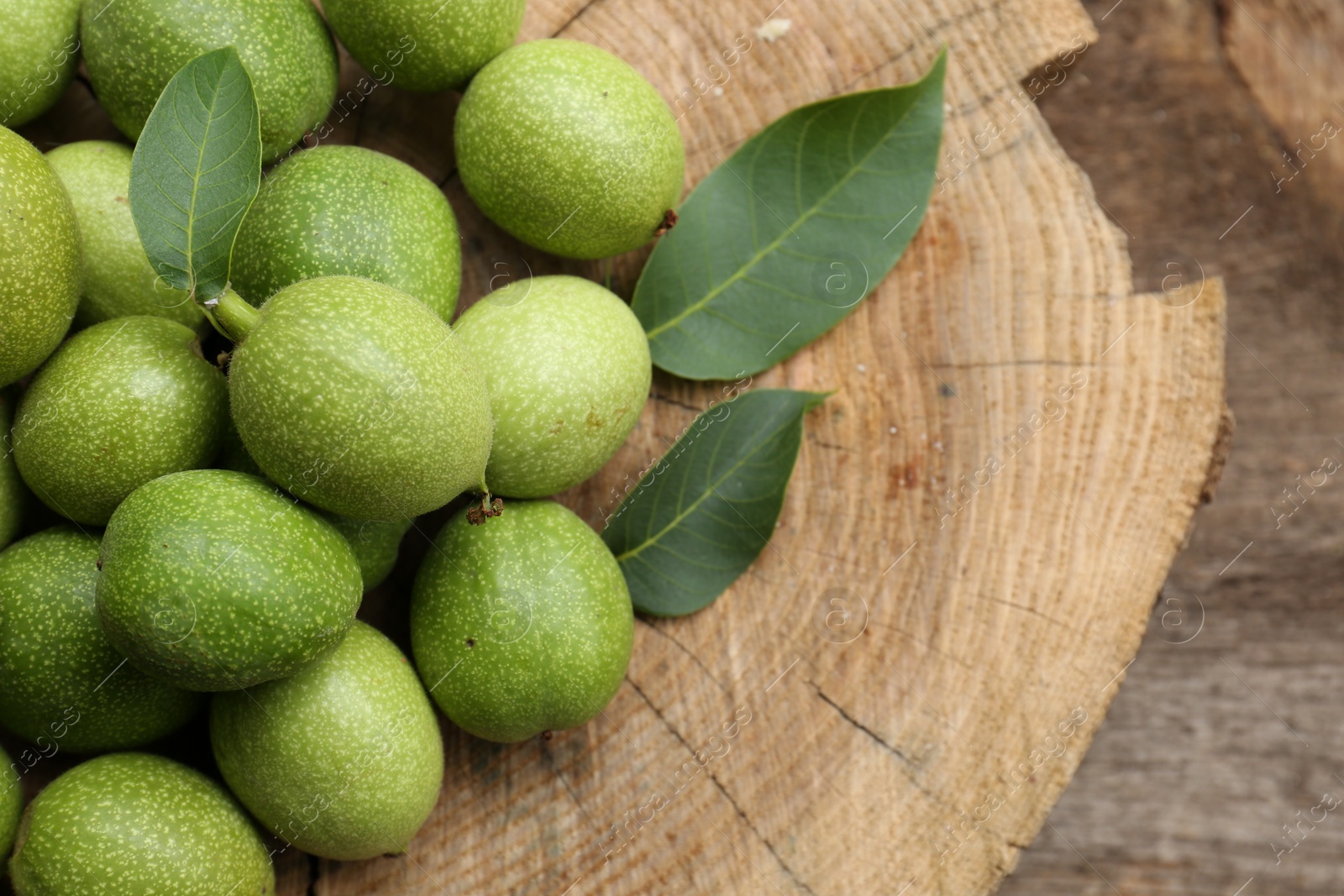 Photo of Many green walnuts and leaves on wooden stump, flat lay