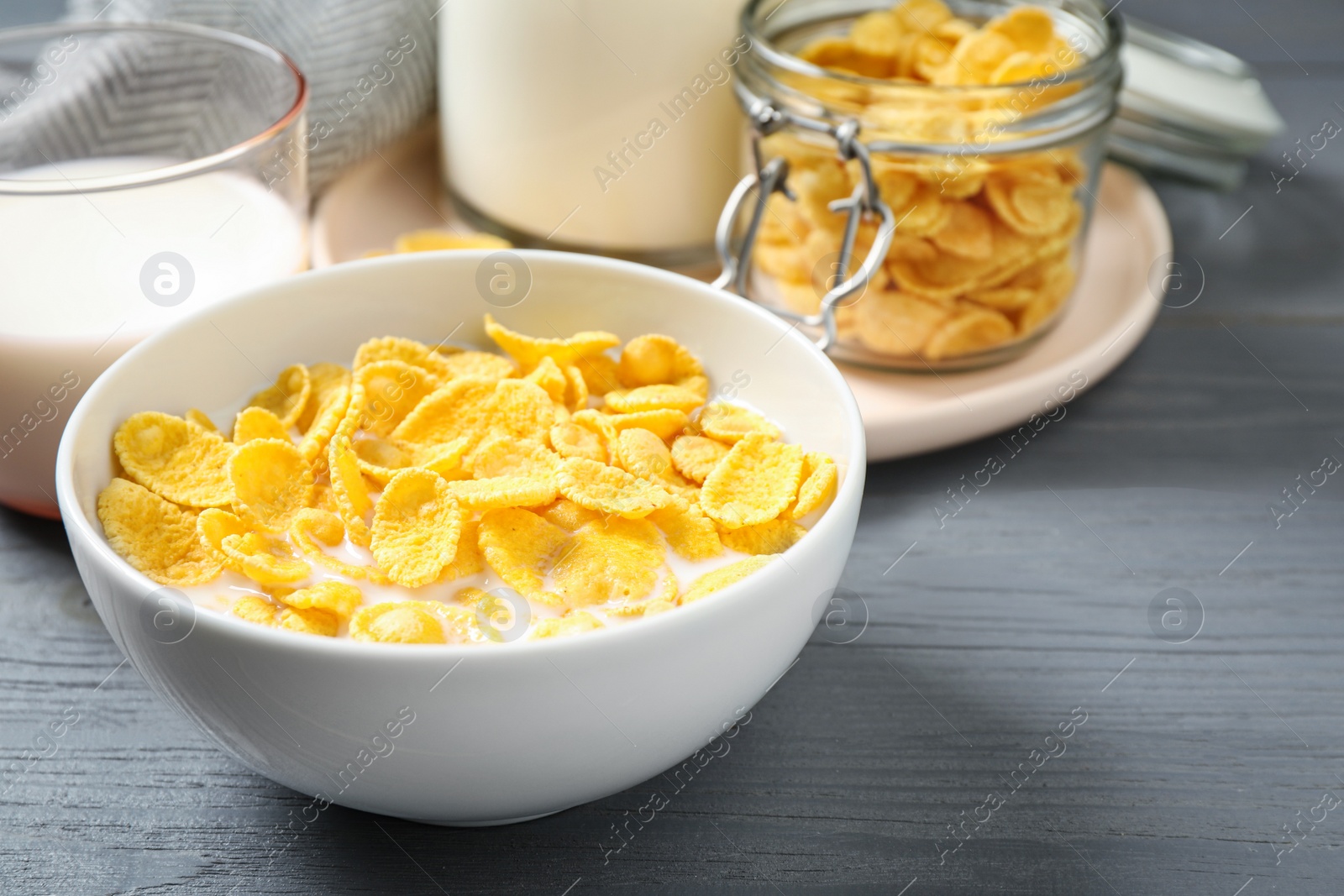 Photo of Tasty crispy corn flakes with milk on grey wooden table