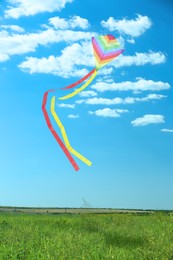 Image of Bright striped rainbow kite flying in blue sky over green grass on sunny day