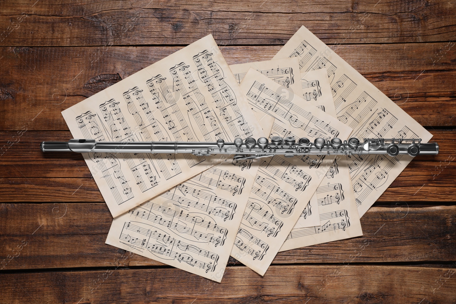 Photo of Sheets with musical notes and flute on wooden table, flat lay