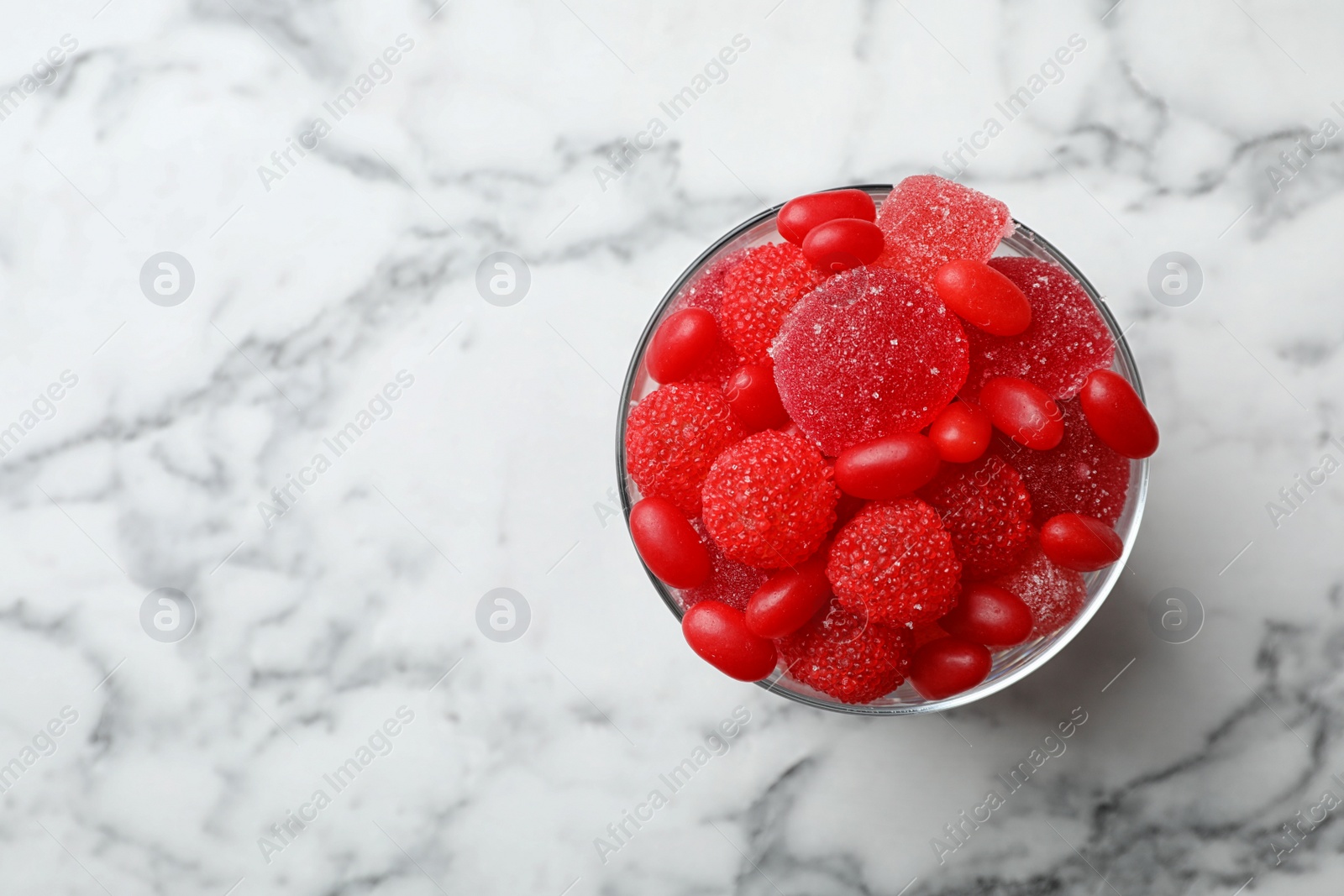 Photo of Glass of delicious chewing candies on marble table, top view with space for text