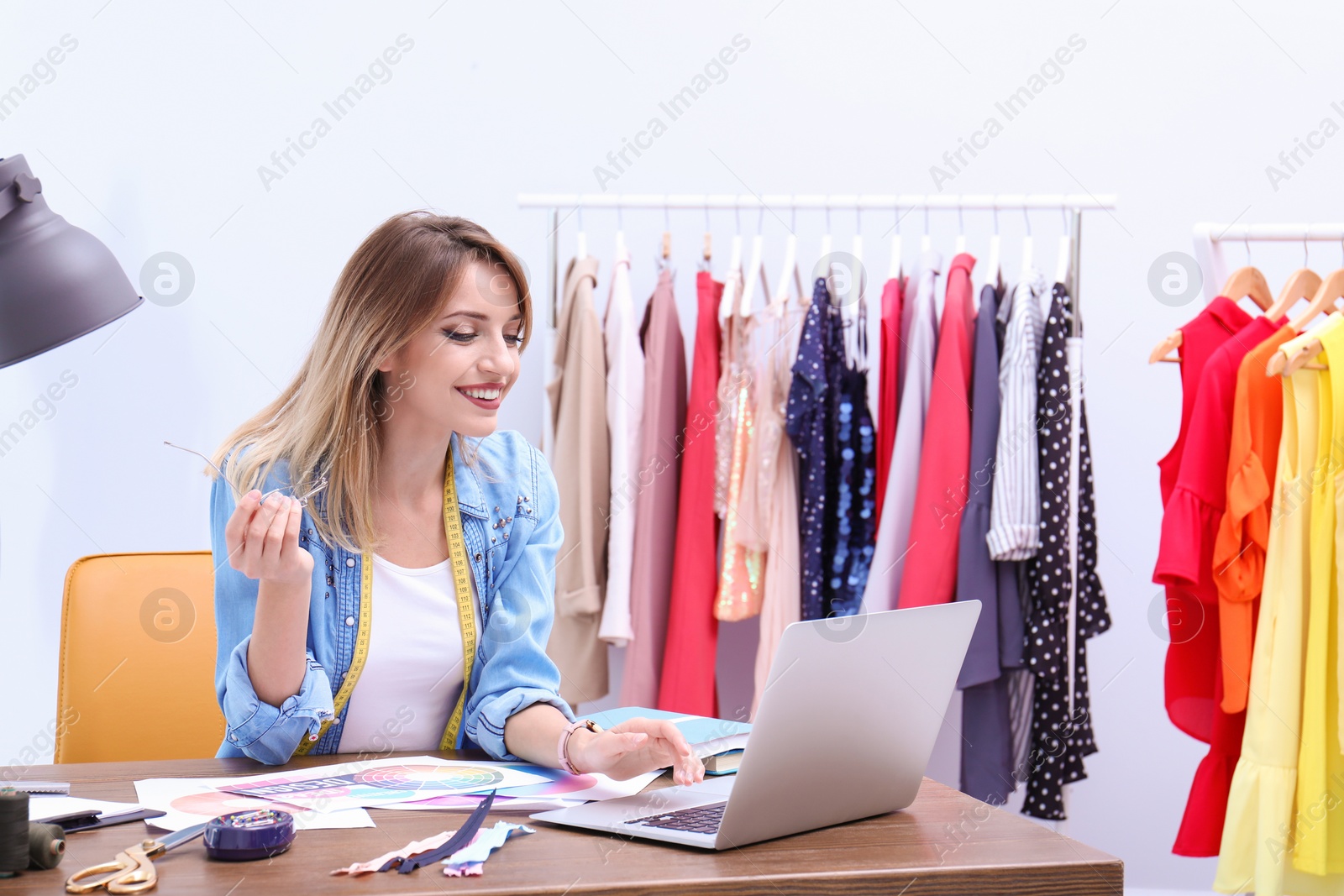 Photo of Beautiful young stylist at workplace near rack with clothes