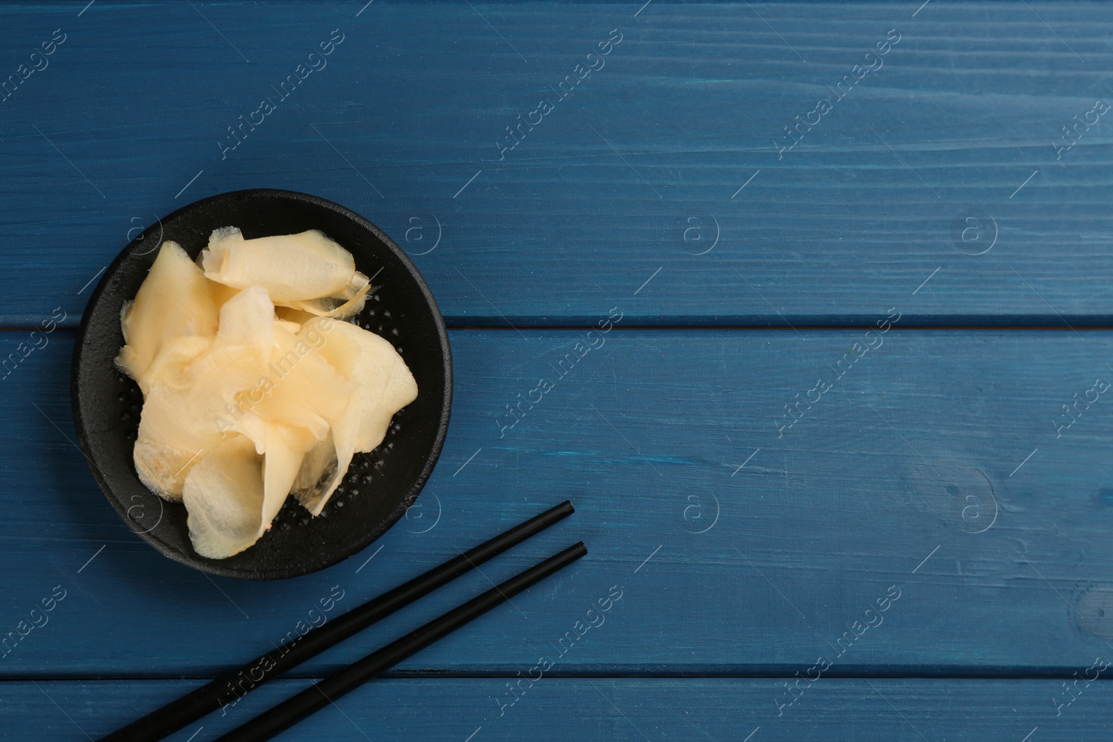 Photo of Spicy pickled ginger and chopsticks on blue wooden table, flat lay. Space for text