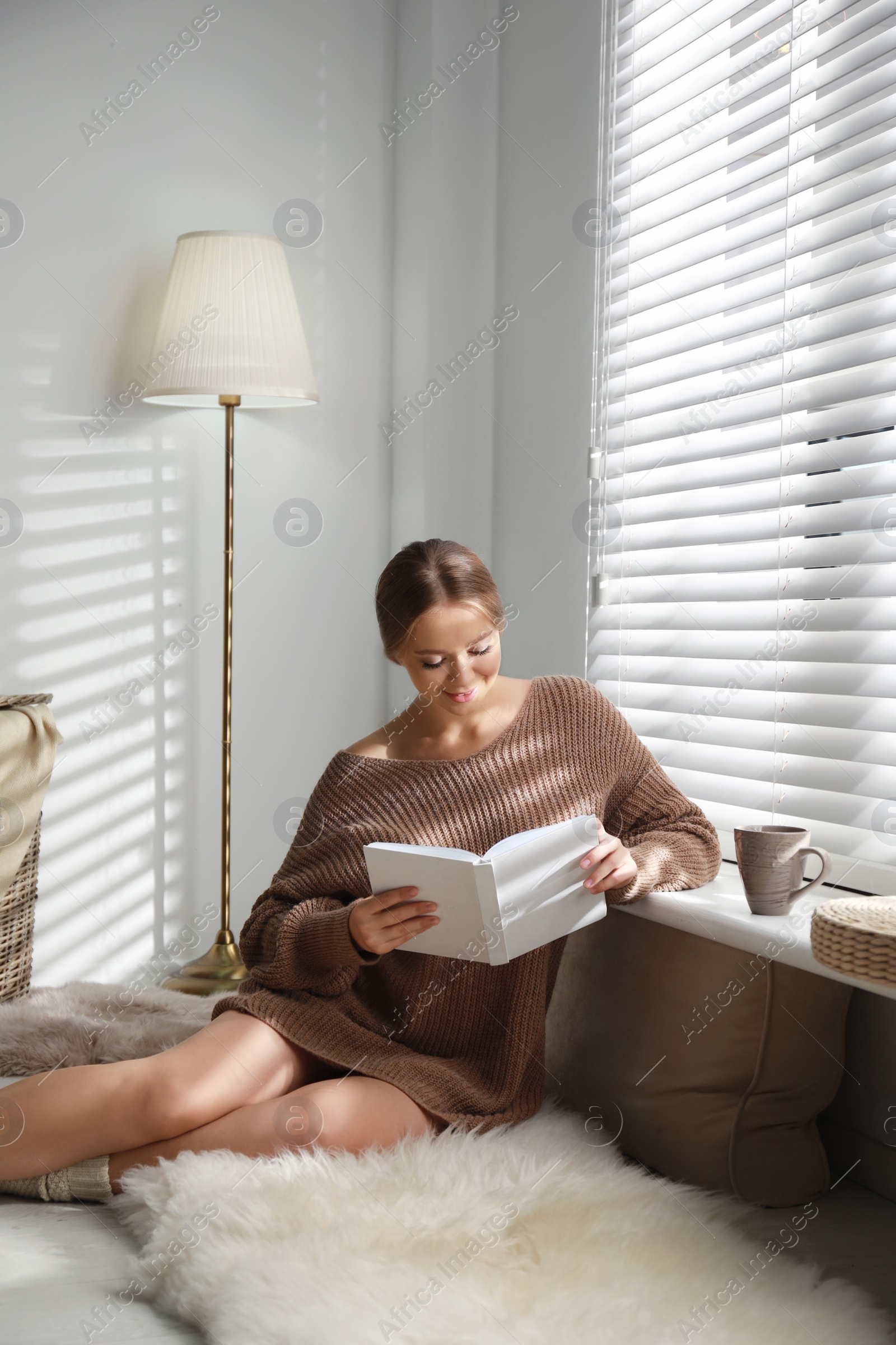 Photo of Beautiful young woman reading book near window at home. Winter atmosphere