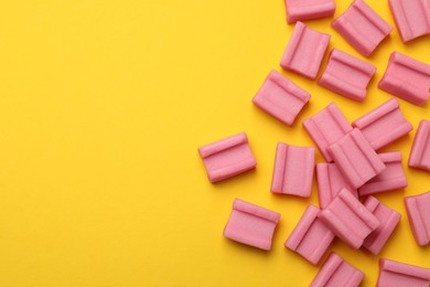 Photo of Tasty pink chewing gums on yellow background, flat lay. Space for text