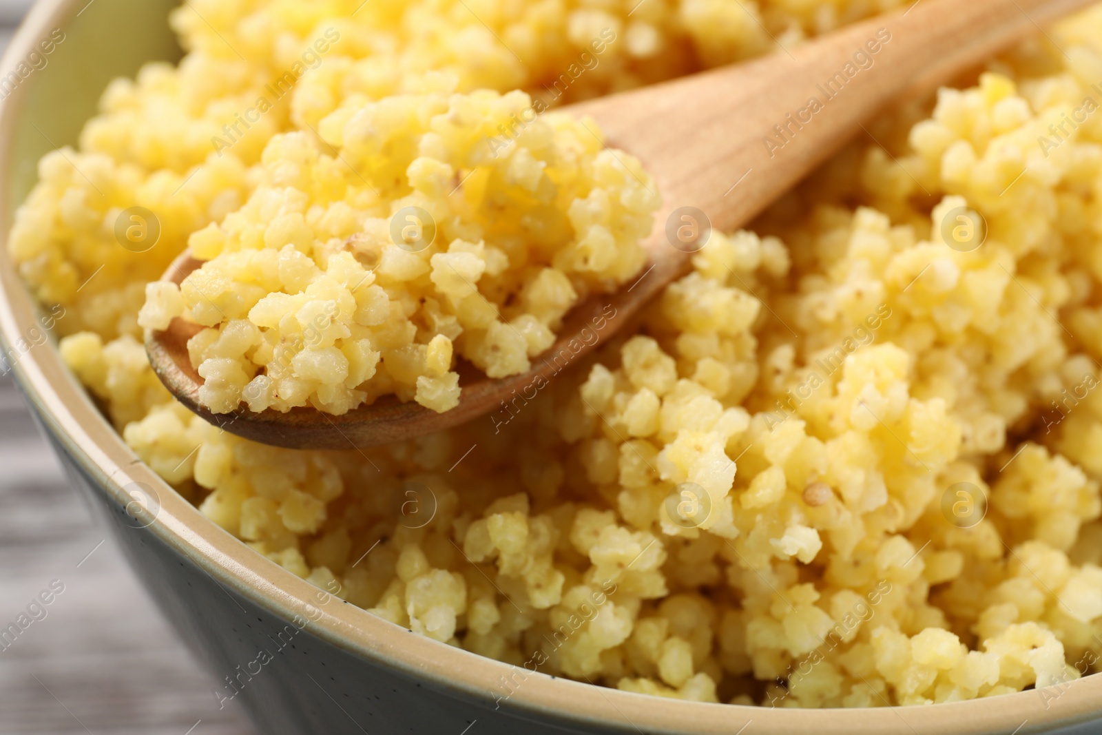 Photo of Tasty millet porridge and spoon in bowl on table, closeup