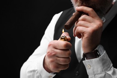 Man lighting cigar on black background, closeup. Space for text