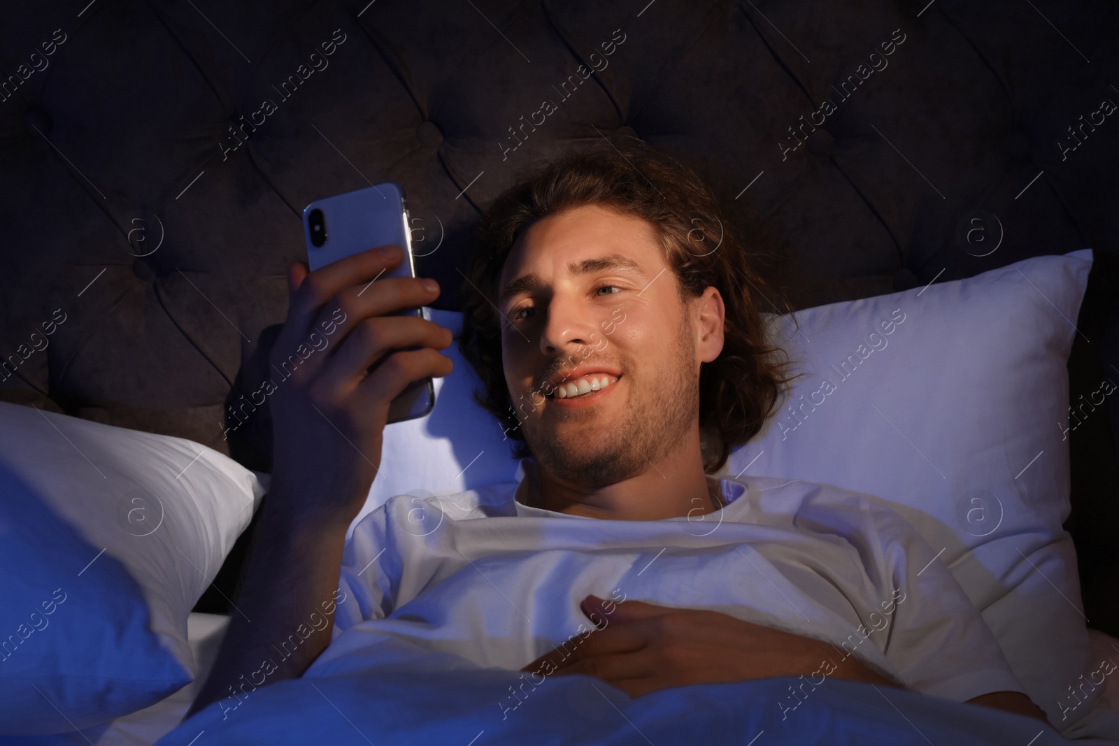 Photo of Handsome young man using smartphone in dark room at night. Bedtime