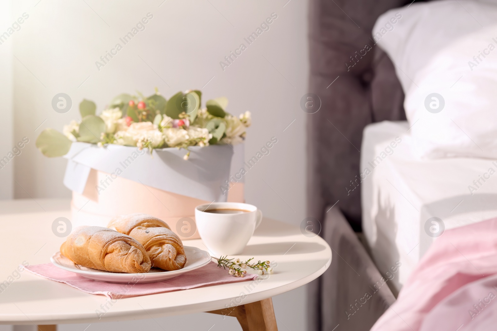 Photo of Plate with delicious croissants and cup of coffee on table near bed