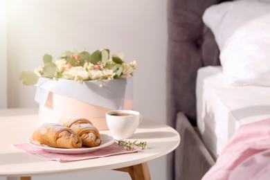 Plate with delicious croissants and cup of coffee on table near bed