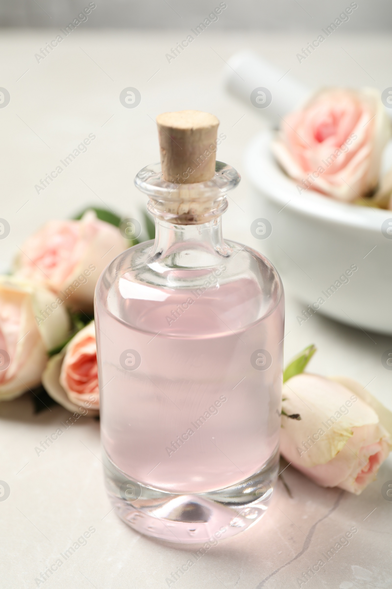 Photo of Bottle of rose essential oil and flowers on white table