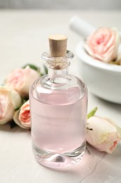 Bottle of rose essential oil and flowers on white table