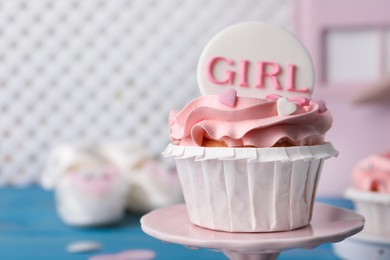 Photo of Delicious cupcake with pink cream and Girl topper for baby shower on stand, closeup