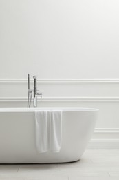 Photo of Modern ceramic bathtub with towel near white wall indoors