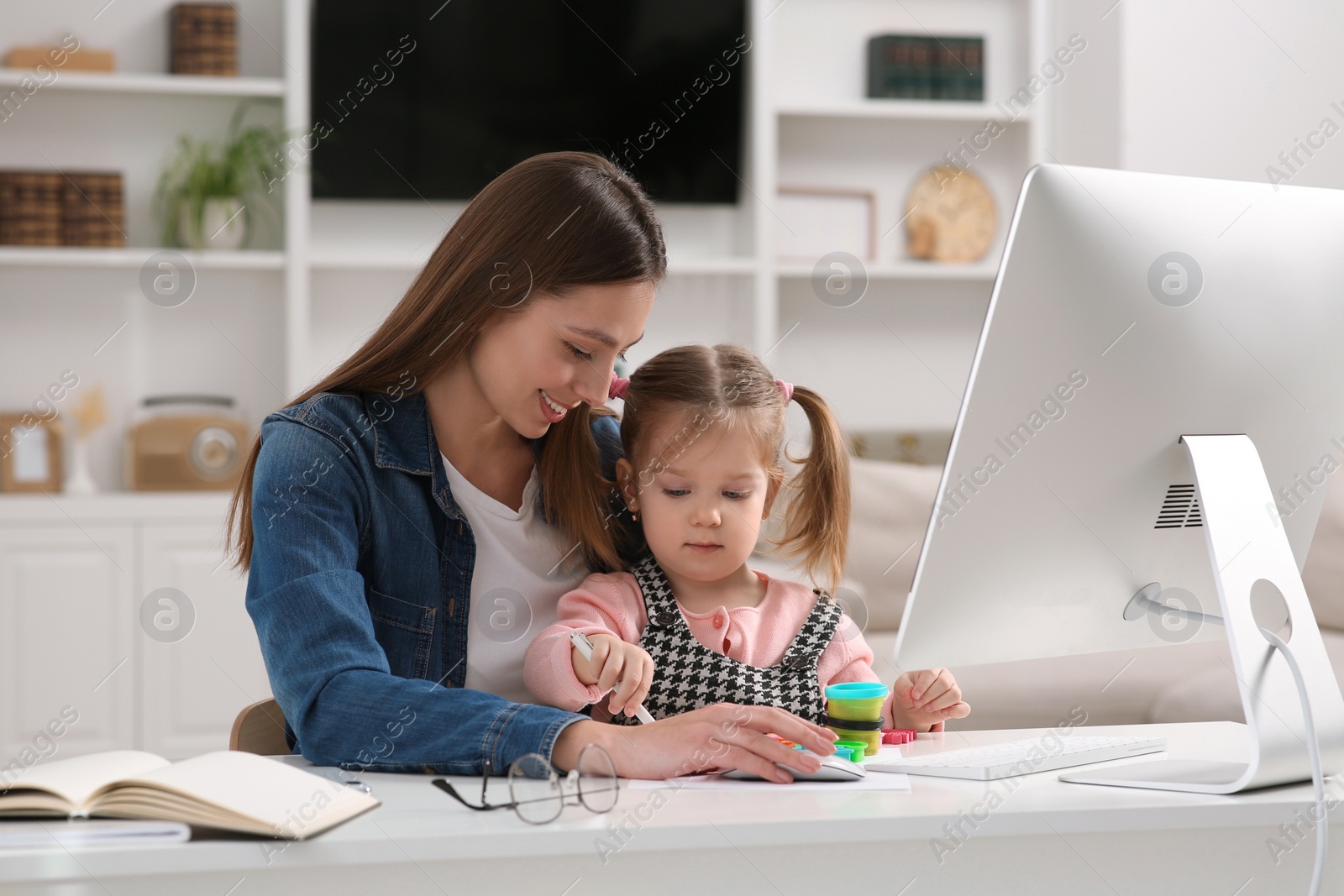 Photo of Woman working remotely at home. Mother and her daughter at desk with computer