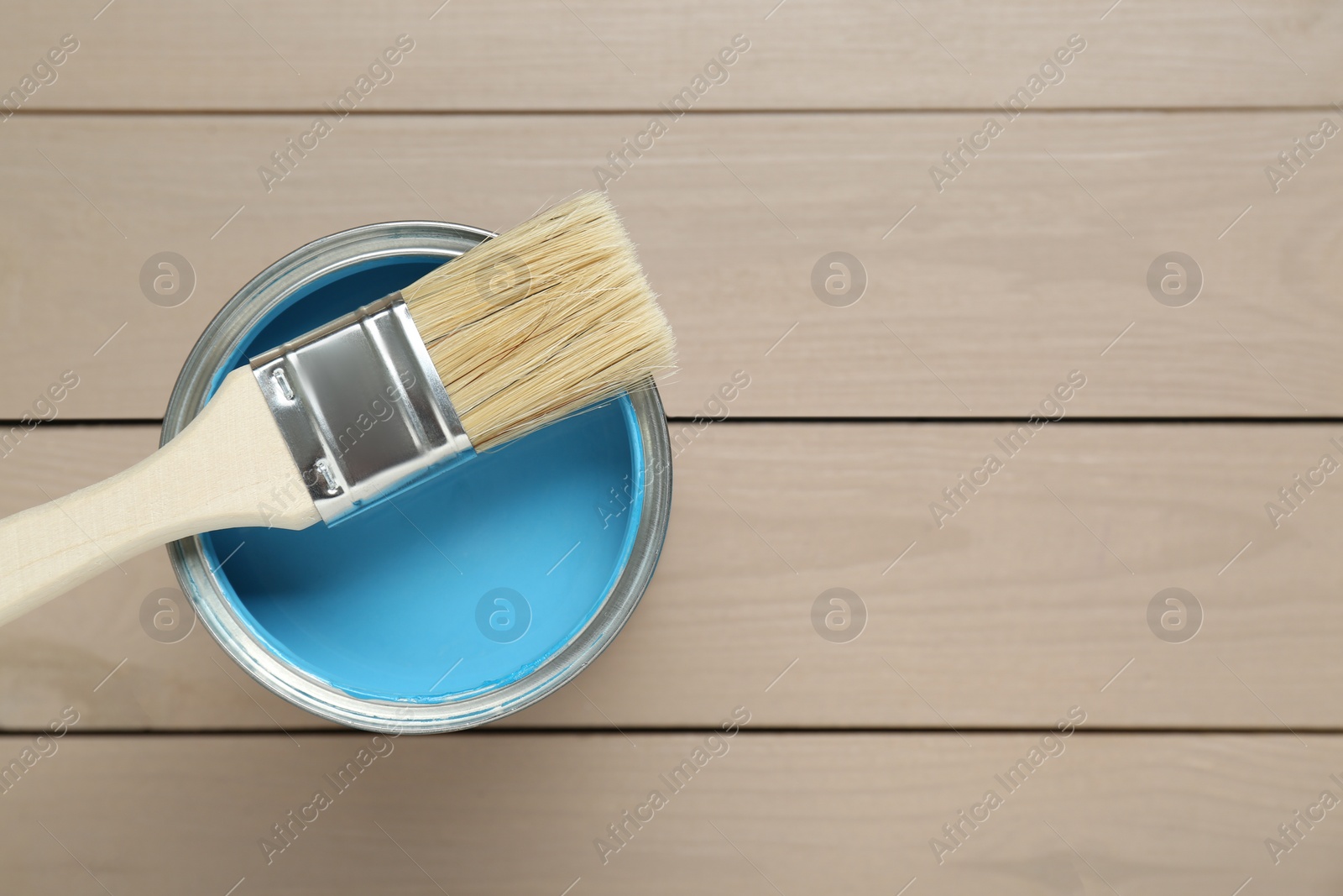 Photo of Can of light blue paint with brush on wooden table, top view. Space for text