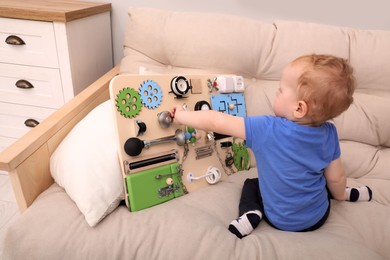 Cute little boy playing with busy board on sofa at home