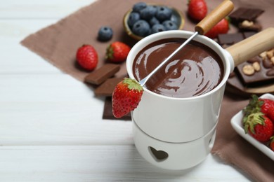 Photo of Fondue pot of melted chocolate and fork with fresh strawberry at white wooden table, space for text