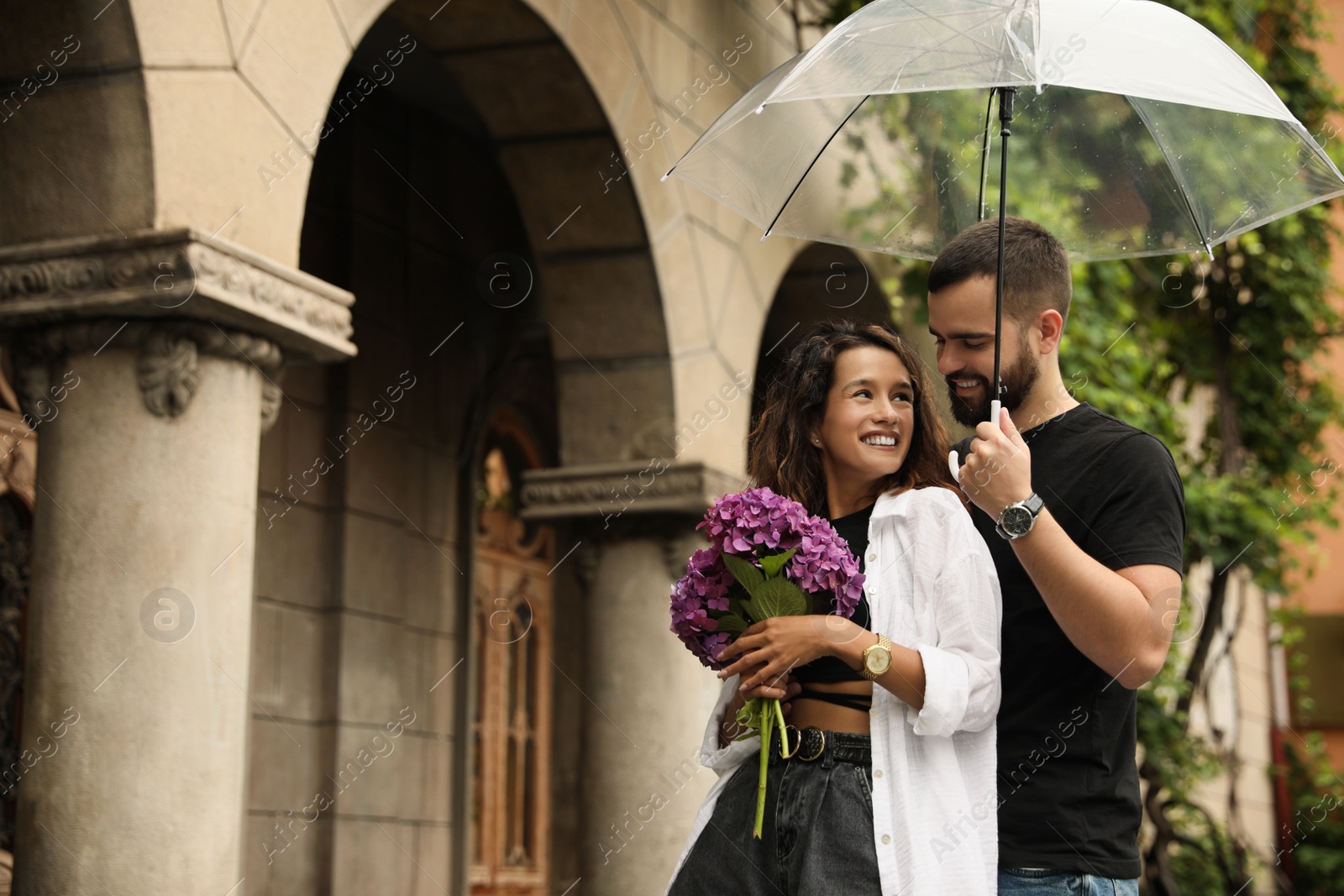 Photo of Young couple with umbrella enjoying time together under rain on city street, space for text