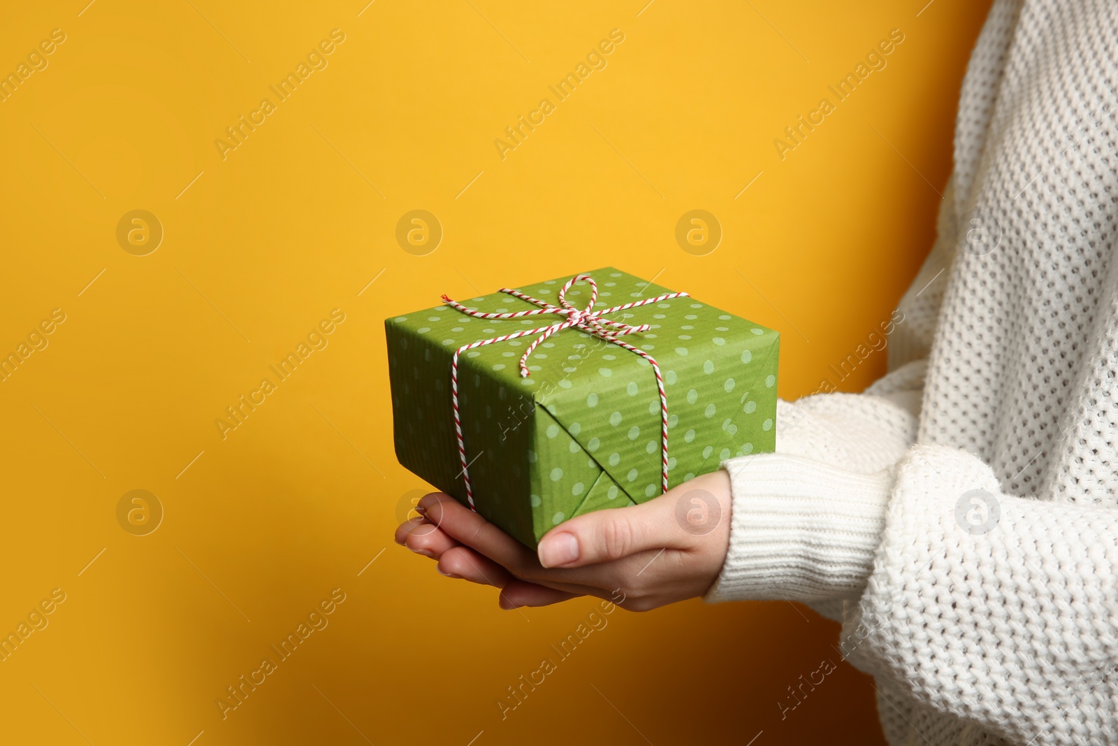 Photo of Woman holding green Christmas gift box on yellow background, closeup