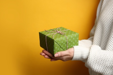 Photo of Woman holding green Christmas gift box on yellow background, closeup