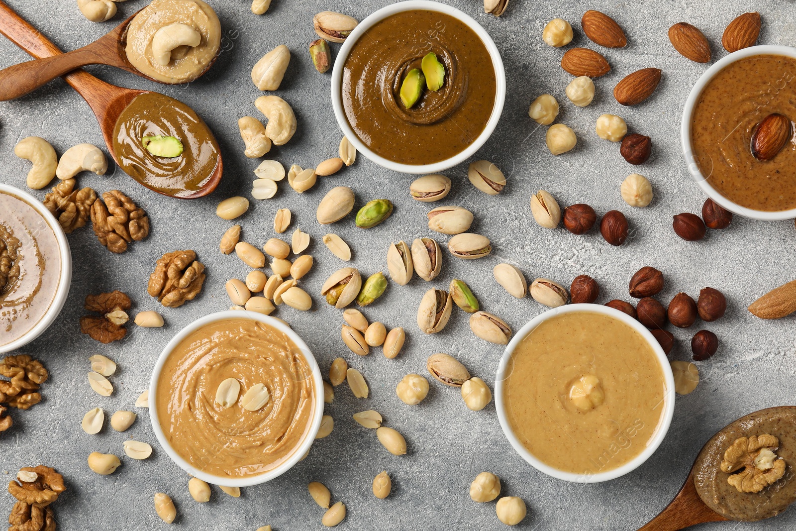 Photo of Tasty nut butters and raw nuts on light grey table, flat lay