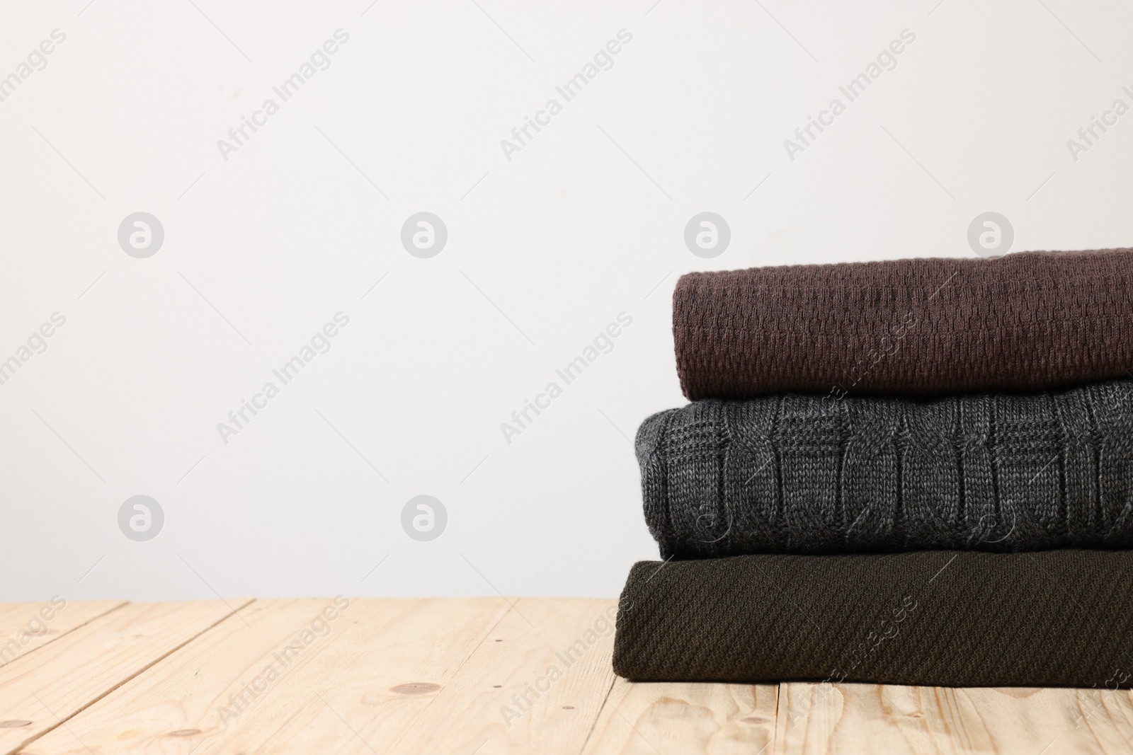 Photo of Stack of casual sweaters on wooden table against light background. Space for text