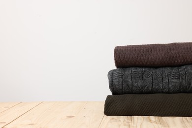 Stack of casual sweaters on wooden table against light background. Space for text