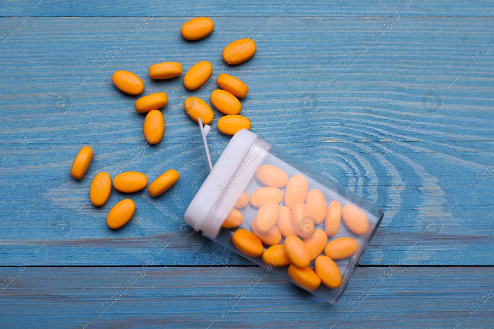 Photo of Tasty dragee candies and container on blue wooden table, flat lay