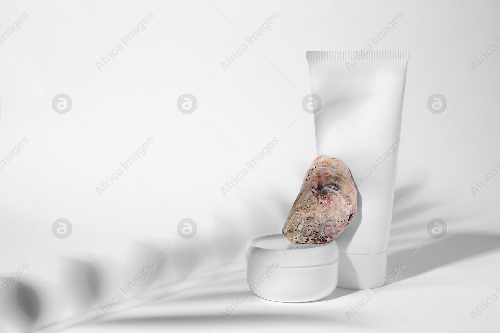 Photo of Cosmetic products, quartz gemstone and shadow of tropical leaf on white background. Space for text