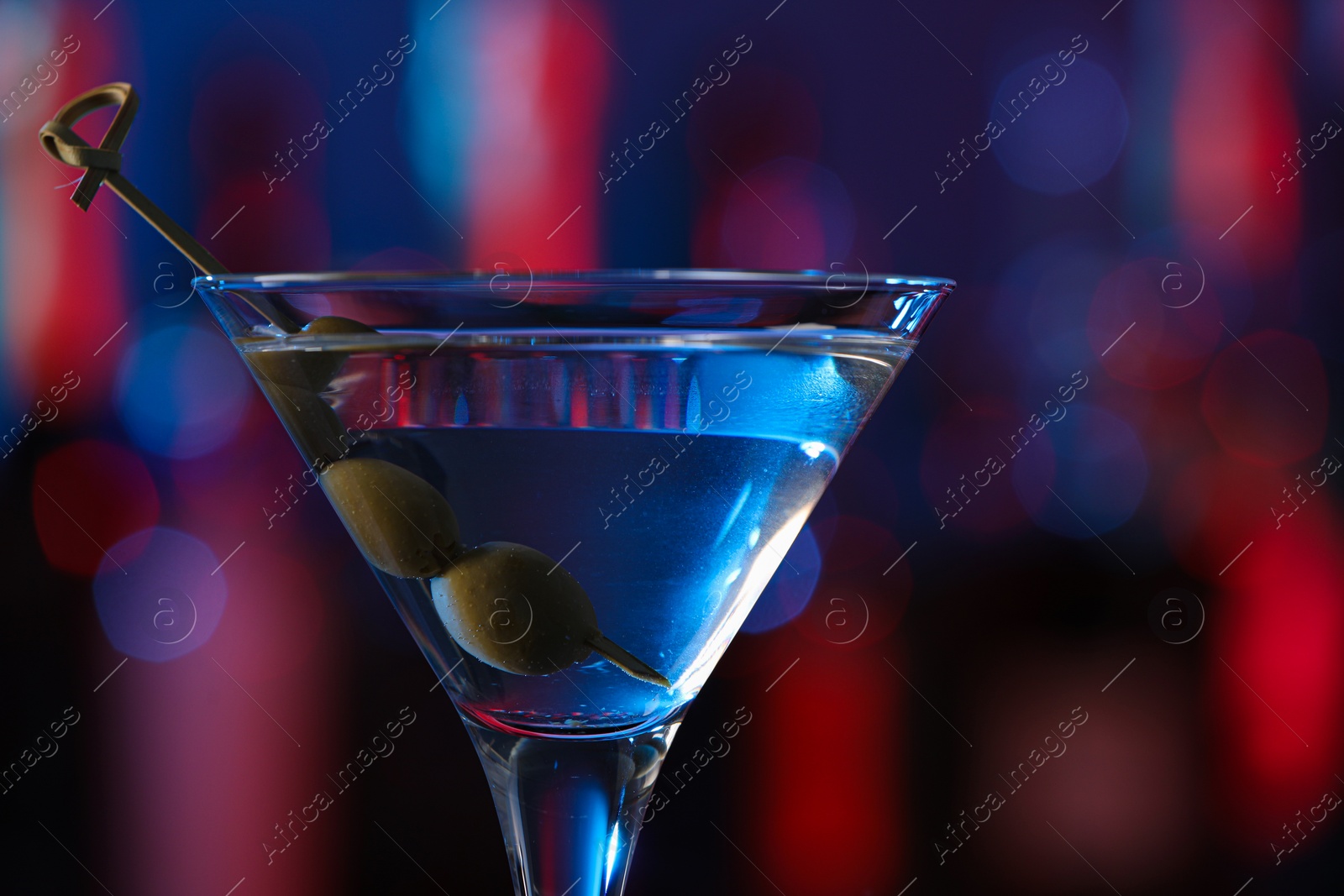 Photo of Martini glass with cocktail and olives in bar, closeup