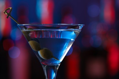 Martini glass with cocktail and olives in bar, closeup