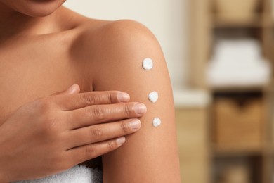 Photo of Young woman applying body cream onto arm indoors, closeup. Space for text