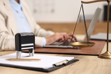 Photo of Notary using laptop at workplace in office, focus on stationery and scales of justice