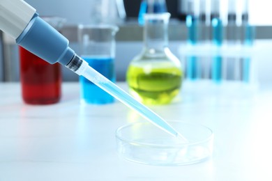 Photo of Laboratory analysis. Micropipette with liquid and petri dish on white table, closeup