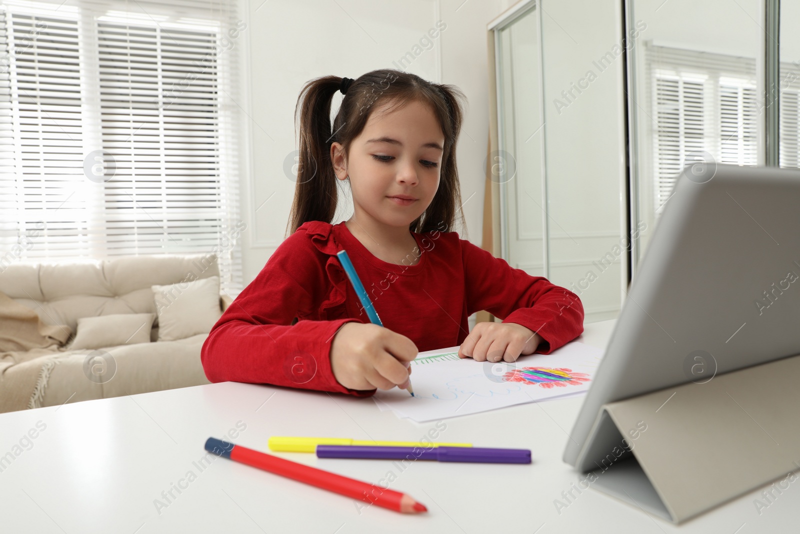 Photo of Little girl drawing on paper with pencil at online lesson indoors. Distance learning