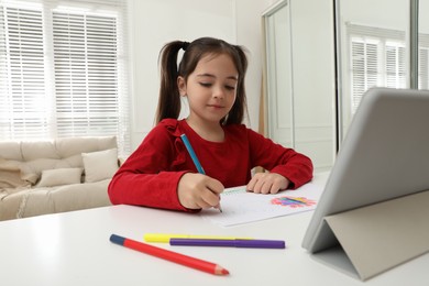 Photo of Little girl drawing on paper with pencil at online lesson indoors. Distance learning