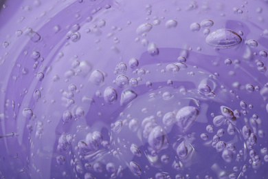 Pure transparent cosmetic gel on lilac background, closeup