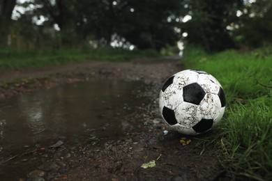 Dirty leather soccer ball near puddle outdoors, space for text