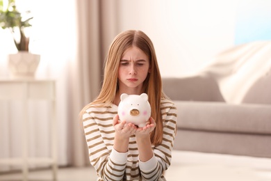 Photo of Sad teen girl with piggy bank at home