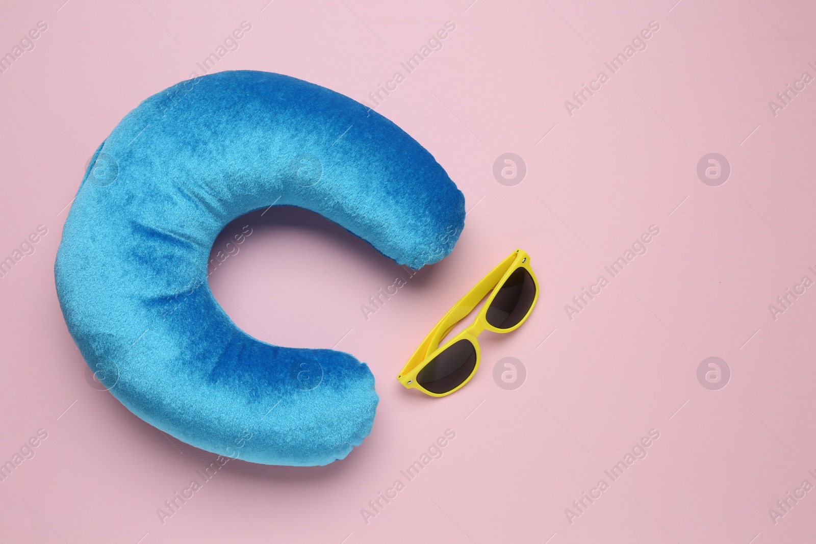 Photo of Light blue travel pillow and sunglasses on pink background, flat lay. Space for text