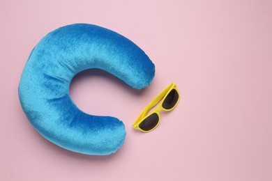 Photo of Light blue travel pillow and sunglasses on pink background, flat lay. Space for text