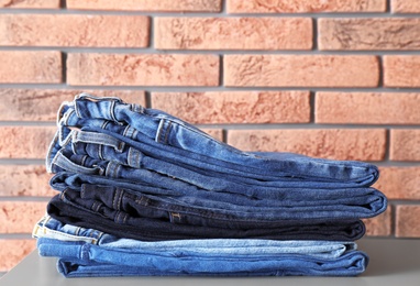 Stack of jeans on table against brick wall background