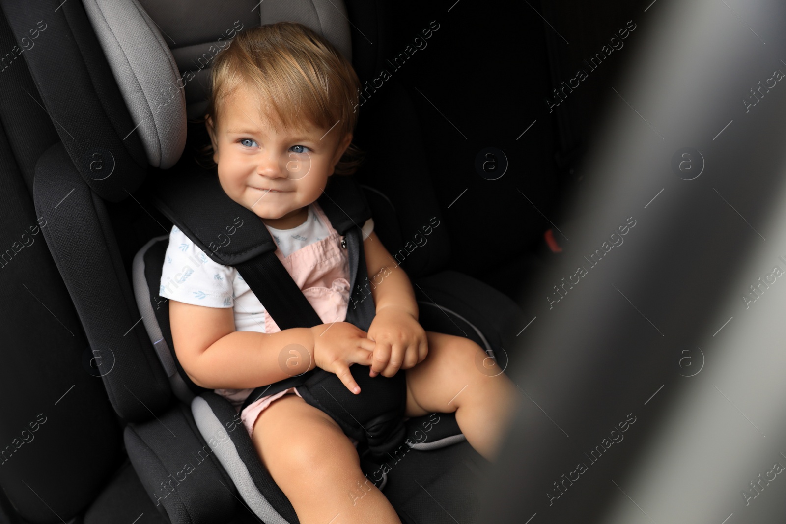 Photo of Cute little girl sitting in child safety seat inside car