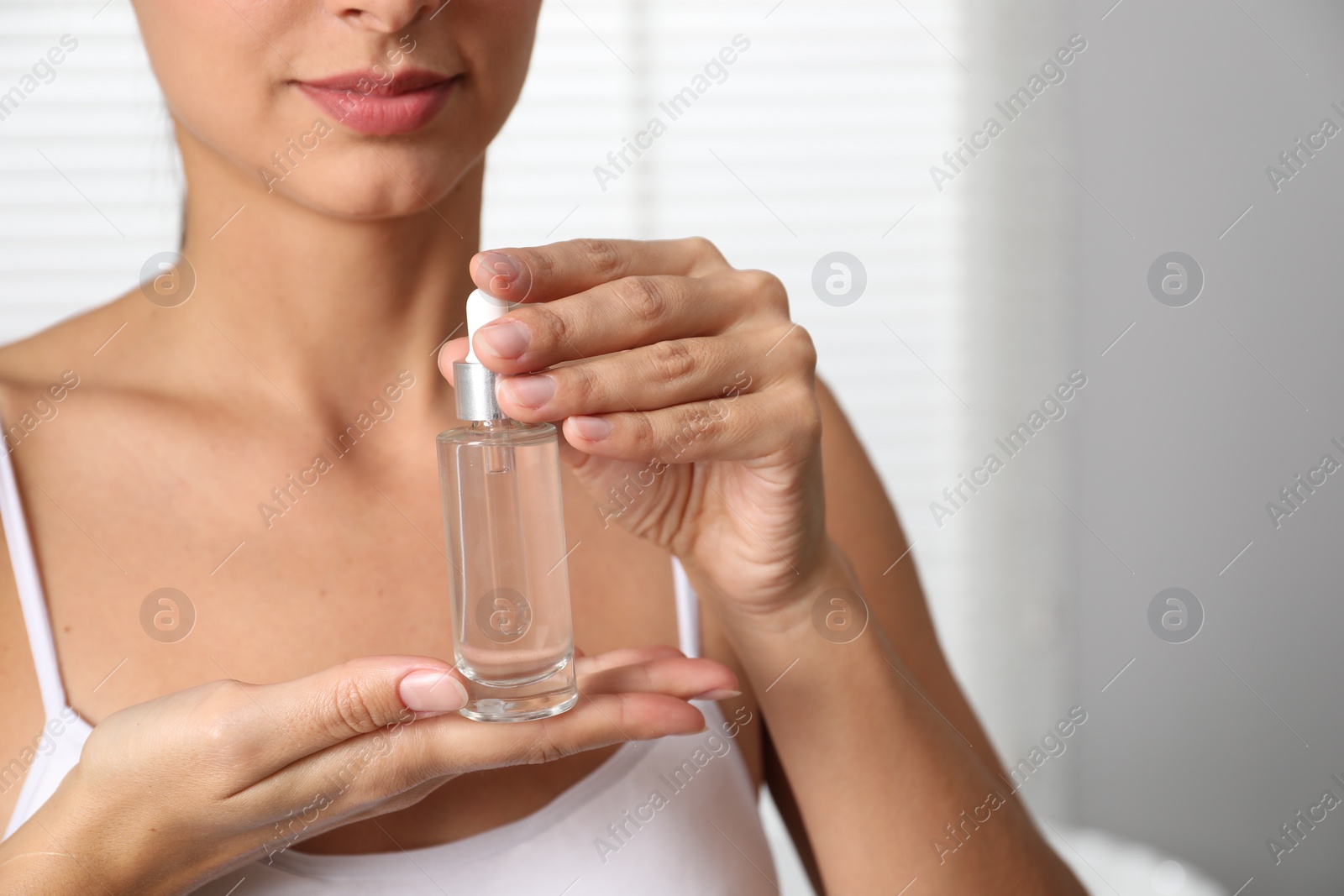 Photo of Woman with bottle of cosmetic serum on blurred background, closeup. Space for text