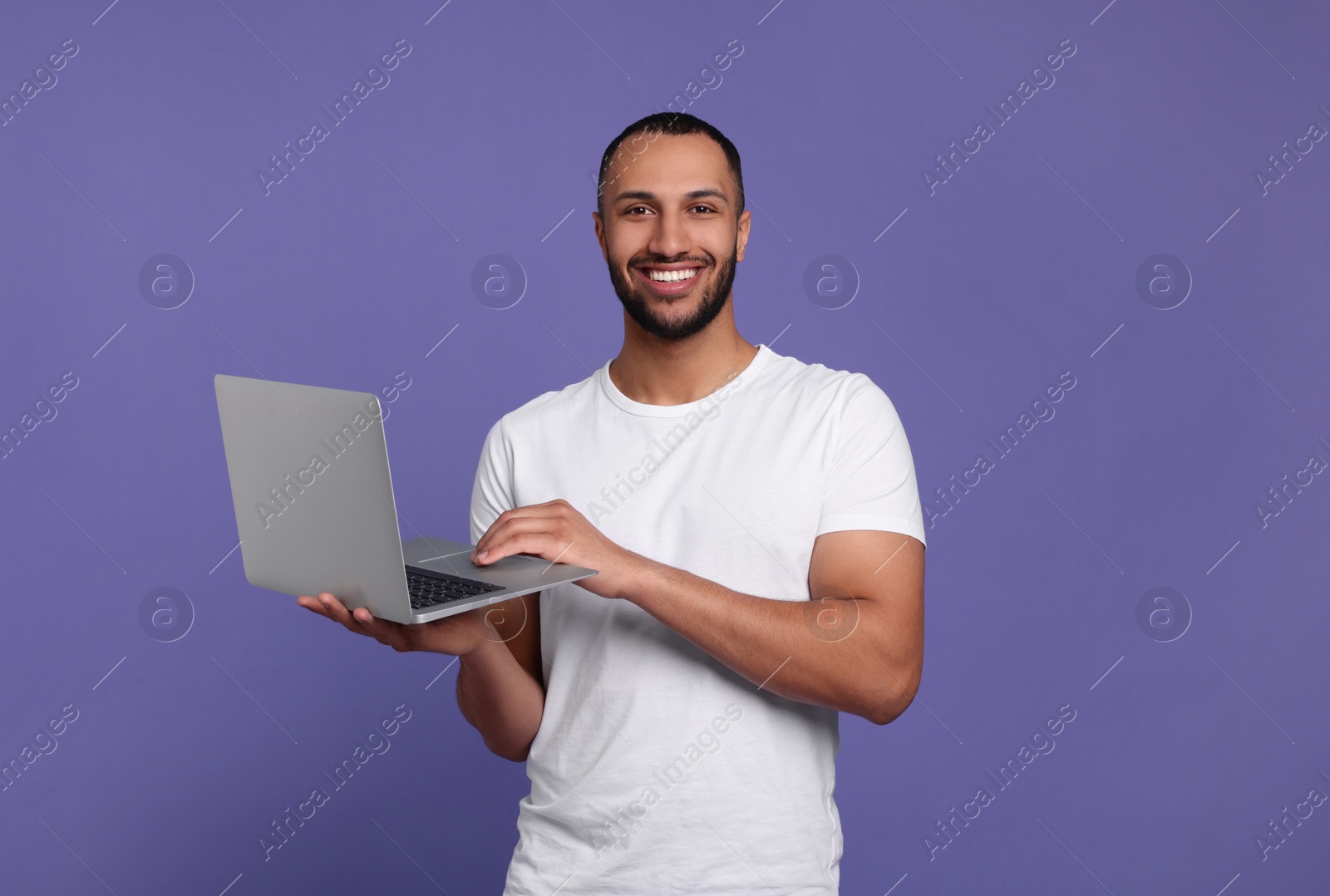 Photo of Smiling young man working with laptop on lilac background