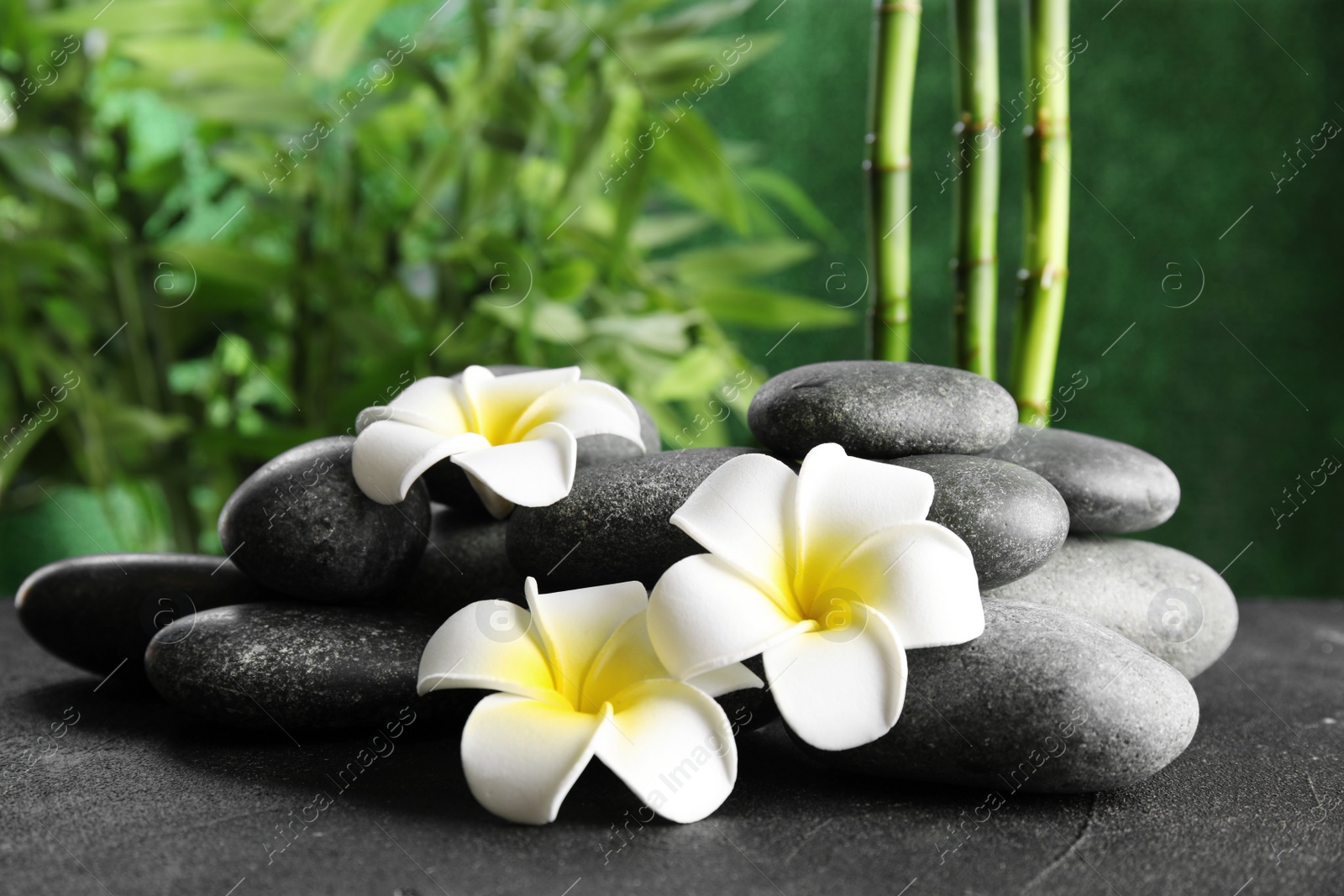 Photo of Zen stones and exotic flowers on table against blurred background