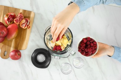 Photo of Woman adding raspberry into blender with ingredients for smoothie at table, top view
