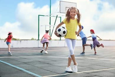 Photo of Cute girl with soccer ball at sports court on sunny day. Summer camp